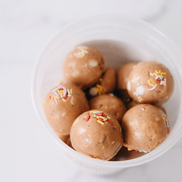 Funfetti Protein bites with sprinkles and white chocolate chips stacked in a plastic container with a white background