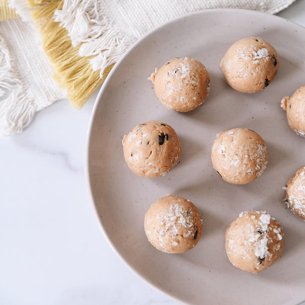 coconut dusted protein bites on a plate with a yellow and white tea towel in the background