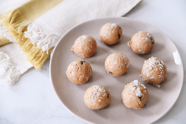 coconut dusted protein bites on a plate with a yellow and white tea towel in the background
